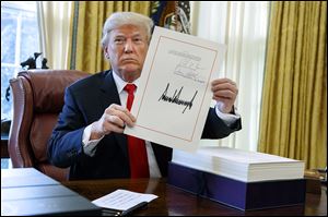 President Donald Trump shows off the tax bill after signing it in the Oval Office of the White House, Friday, Dec. 22, 2017.