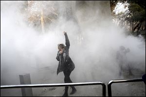 A university student attends a protest inside Tehran University while a smoke grenade is thrown by anti-riot Iranian police in Tehran, Iran, on Dec. 30.