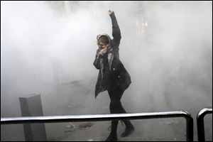A student attends a protest inside Tehran University in Iran while a smoke grenade is thrown by Iranian police.