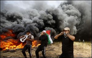 Palestinian protesters chant slogans next to burning tires during clashes with Israeli troops along Gaza's border with Israel, east of Khan Younis, Gaza Strip.