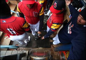 Mud Hens players huddle around a heater in the dugout during Saturday's game at Fifth Third Field. Toledo's contest with Pawtucket on Sunday was postponed by rain and cold weather.