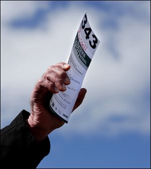 A man holds up his ticket to bid on a car at a Toledo Police Department auction in 2015. An auction held Saturday netted more than $97,000.